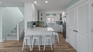 Une cuisine moderne avec des meubles blancs, un îlot central doté de tabourets et un escalier avec des marches à motifs.