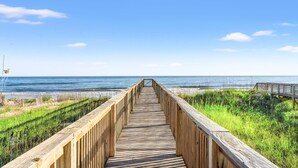 Une promenade en bois qui mène à une plage, avec un ciel dégagé.