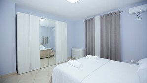 Een hotelkamer met een bed, een kledingkast, een spiegel, een nachtkastje en een raam met gordijnen.