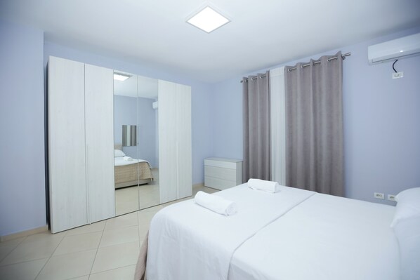Ein Hotelzimmer mit Bett, Kleiderschrank, Spiegel, Nachttisch und einem Fenster mit Vorhängen.