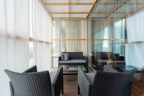 Ein modernes Zimmer mit Korbmöbeln, einem Glastisch und großen Fenstern mit durchsichtigen Vorhängen.