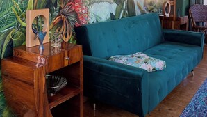 A living room with a teal sofa, wooden side table, and a mural of a tropical scene. - Design apartment in the Sternkopf-Engel-Villa (Oederan)