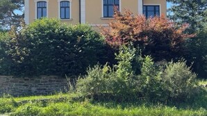 A two-story house with a gabled roof, a stone wall in front, and a clear blue sky. - Design apartment in the Sternkopf-Engel-Villa (Oederan)