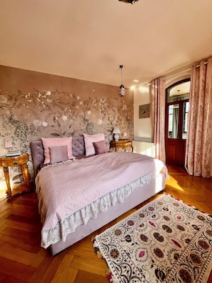 A bedroom with a bed, a nightstand, a lamp, a patterned rug, and a floral wallpaper.