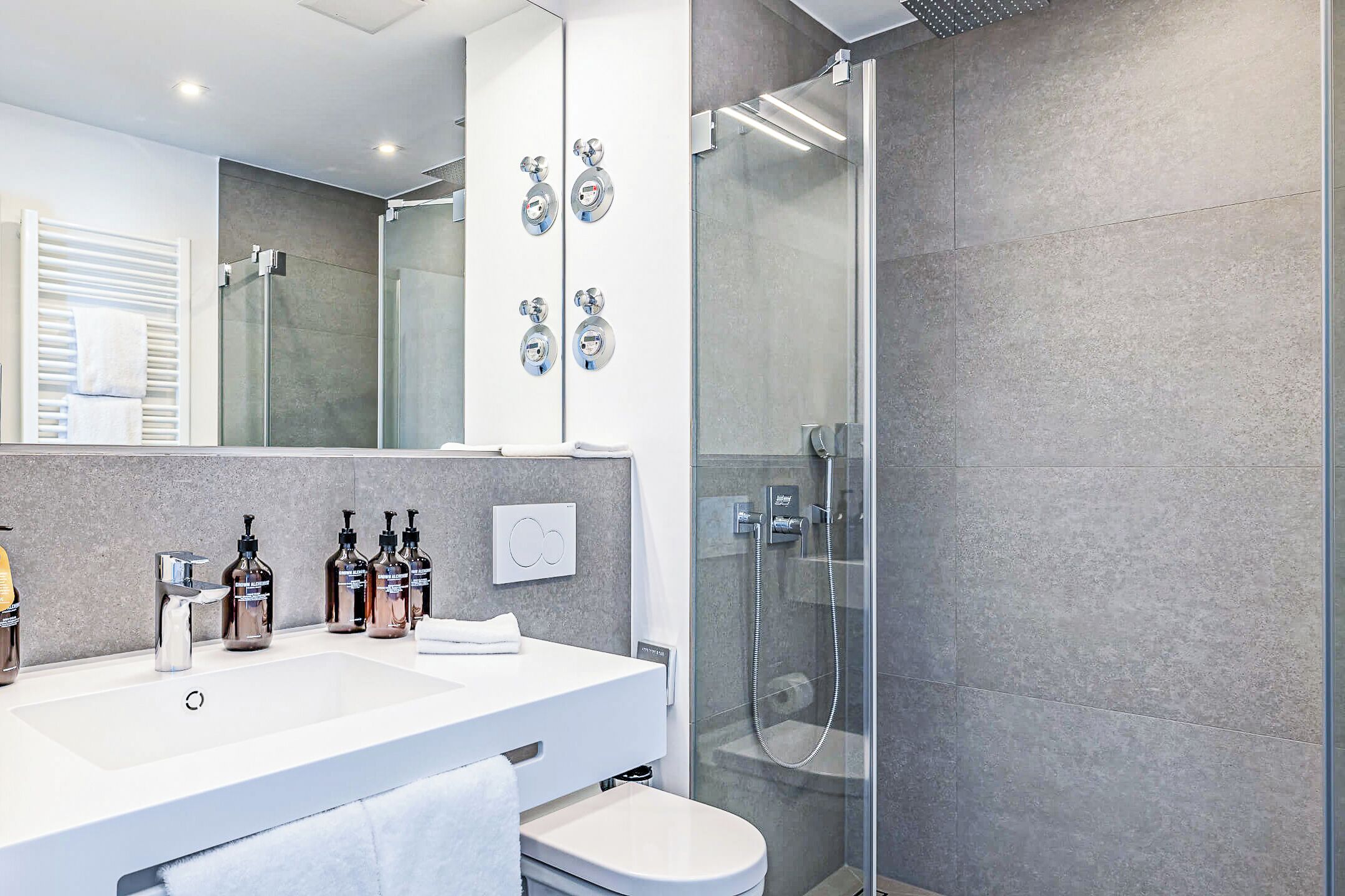 Ein modernes Badezimmer mit einer gläsernen Dusche, einem weißen Waschbecken und einem großen Spiegel.