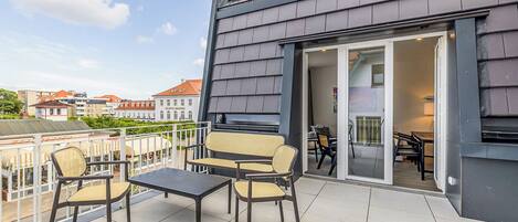 A balcony with a table and chairs, a sliding glass door leading to an interior space, and a view of surrounding buildings.