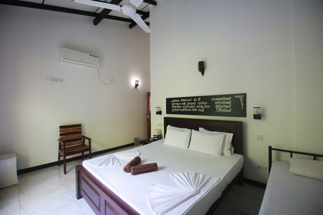 A hotel room with a bed, a chair, a wall-mounted air conditioner, and a signboard with text.