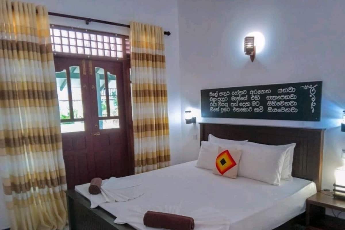 A neatly made bed with white linens and a brown towel, a wooden headboard, and a wall-mounted light fixture.