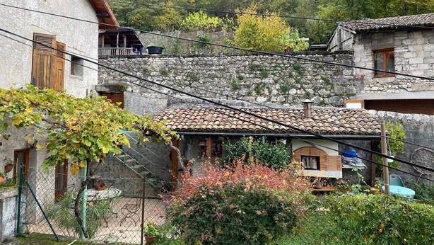 Un bâtiment rustique en pierre, doté d’un toit en tuiles, entouré d’une végétation luxuriante et d’un mur de pierre.