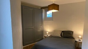 Une chambre à coucher comprenant un lit, deux tables de chevet avec des lampes, une armoire et une fenêtre laissant entrer la lumière naturelle.