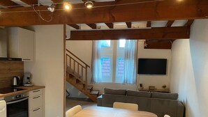 Eine moderne Küche mit Holzbalken, einem Essbereich mit Tisch und Stühlen, einem eingebauten Backofen und einem an der Wand befestigten Fernseher.