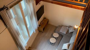 Ein gemütliches Wohnzimmer mit einer Couch, zwei runden Tischen, einem Fernseher und einer Holzbalkendecke.