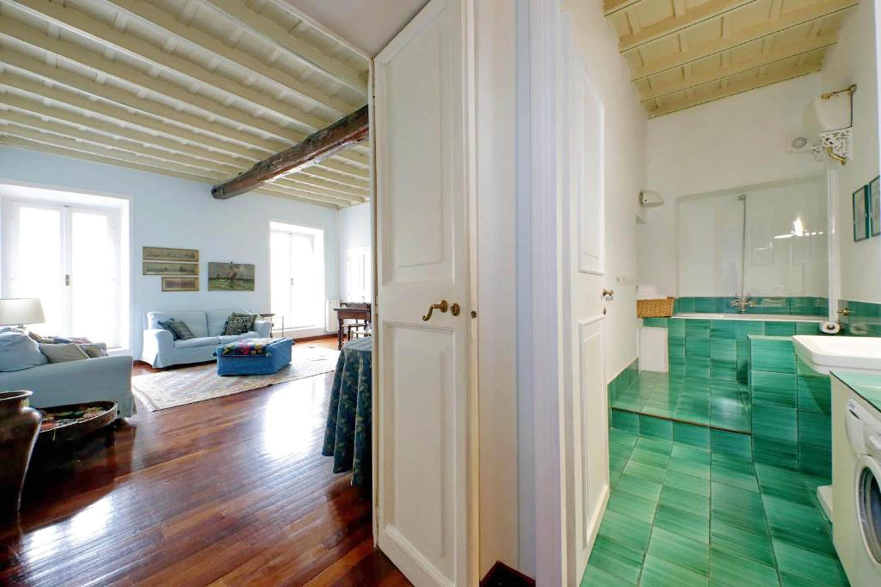 A room with a wooden floor, a white door, a blue sofa, and a green tiled bathroom.