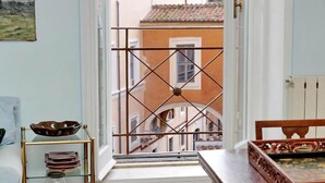 A room with a window overlooking a building, a wooden table, and a shelf with decorative items. - Flatinrome Spagna Spanish Steps (ROMA)