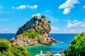 A rocky island with a building on top, surrounded by clear blue waters and greenery.