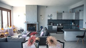Una sala de estar moderna con chimenea, una cocina con armarios grises y un comedor con mesa y sillas.