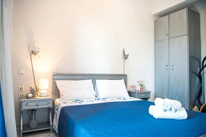 Un lit bien fait, avec une couvre-lit bleue et des oreillers blancs, une lampe de chevet, une petite table avec une lampe et une armoire.