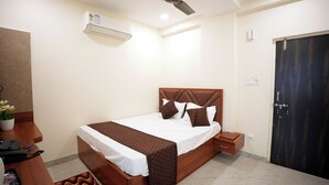 A neatly arranged bedroom with a bed, bedside tables, a nightstand, a potted plant, and a door. - HOTEL CITY INN (Nagpur)