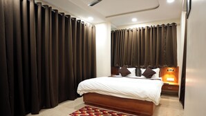 A bedroom with a bed, curtains, a nightstand, and a wall-mounted lamp. - HOTEL CITY INN (Nagpur)