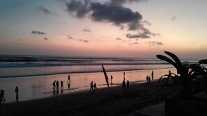 Ein Strandbild, aufgenommen bei Sonnenuntergang, zeigt Personen, die am Ufer entlanggehen.