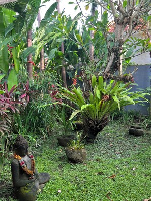Ein Garten mit einer Buddha-Statue, üppigem Grün und verschiedenen Pflanzen.