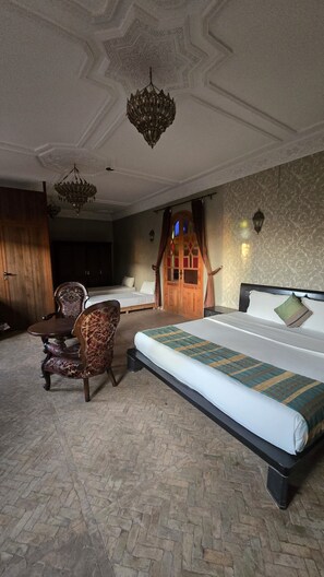 A bedroom with a large bed, a wooden chair, a desk, and a chandelier.