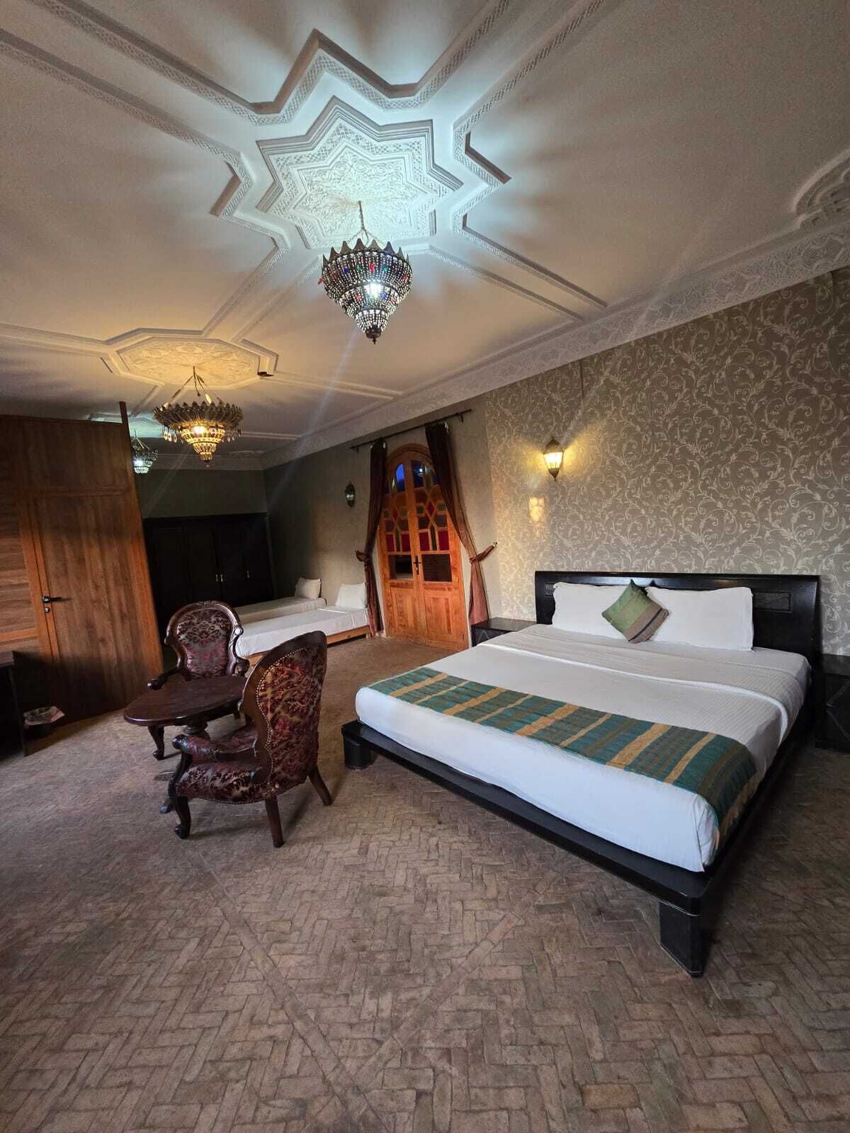 A hotel room with a large bed, a desk, a chair, and a chandelier.