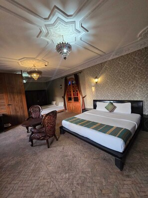 A hotel room with a large bed, a desk, a chair, and a chandelier.