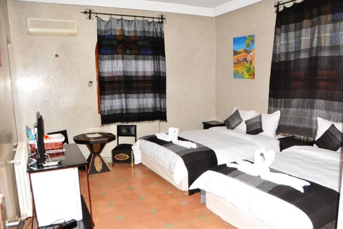 A hotel room with two beds, a desk with a computer, a small table, and a chair.