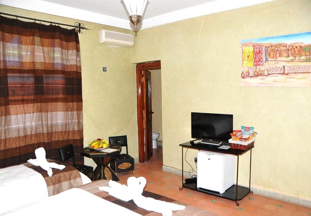 Une chambre d’hôtel avec un lit, une télévision, une petite table avec des en-cas, une chaise et un tableau au mur.