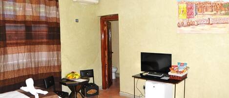 Une chambre d’hôtel avec un lit, une télévision, une petite table avec des en-cas, une chaise et un tableau au mur.