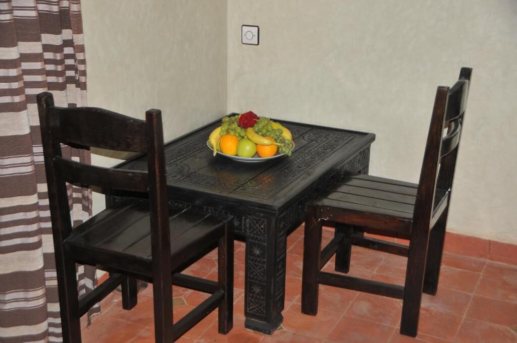 A dining table with a fruit bowl, two chairs, and a patterned tablecloth.