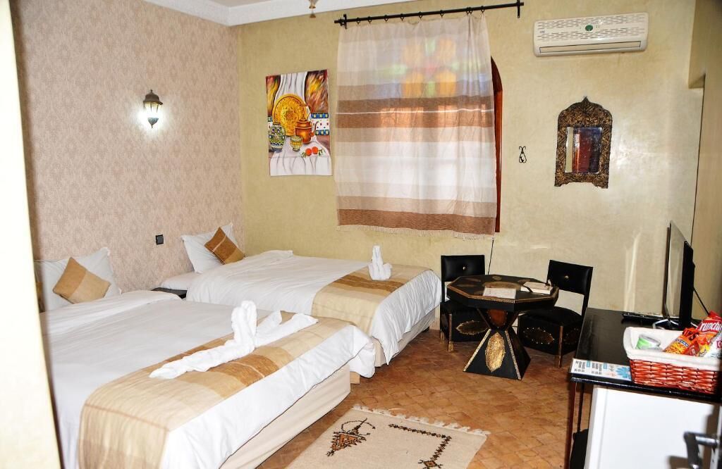 Ein Hotelzimmer mit zwei Betten, einem Esstisch, Stühlen, einem kleinen Kühlschrank und einer Wandklimaanlage.