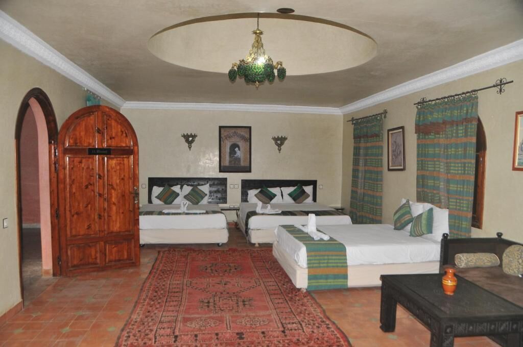 Habitació d'hotel amb dos llits, un armari de fusta, un penjador de cristall i una catifes amb dibuixos.