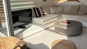 Een moderne woonkamer met een bank, een rond bijzettafeltje, een rieten pouf en een open haard.