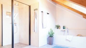 Un baño moderno con mampara de vidrio, bañera y una planta en maceta.