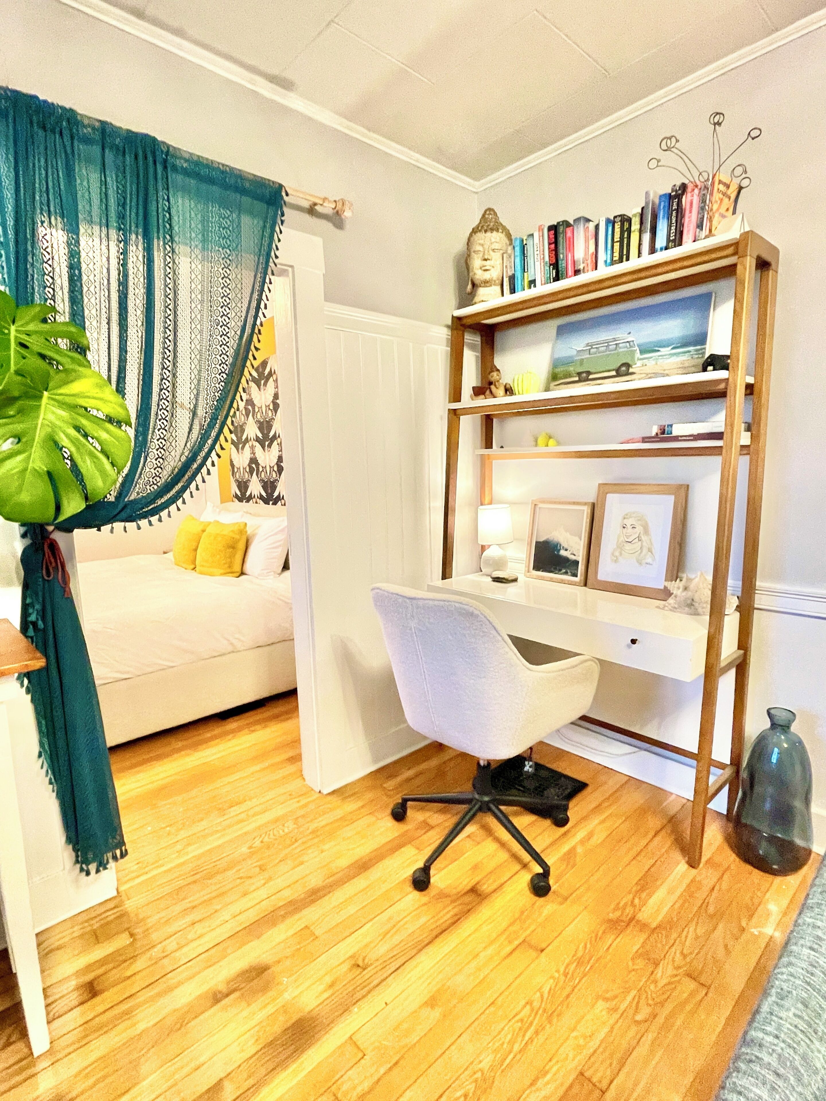 Una habitación con un sofá blanco, un escritorio con una silla, una estantería y una planta grande.
