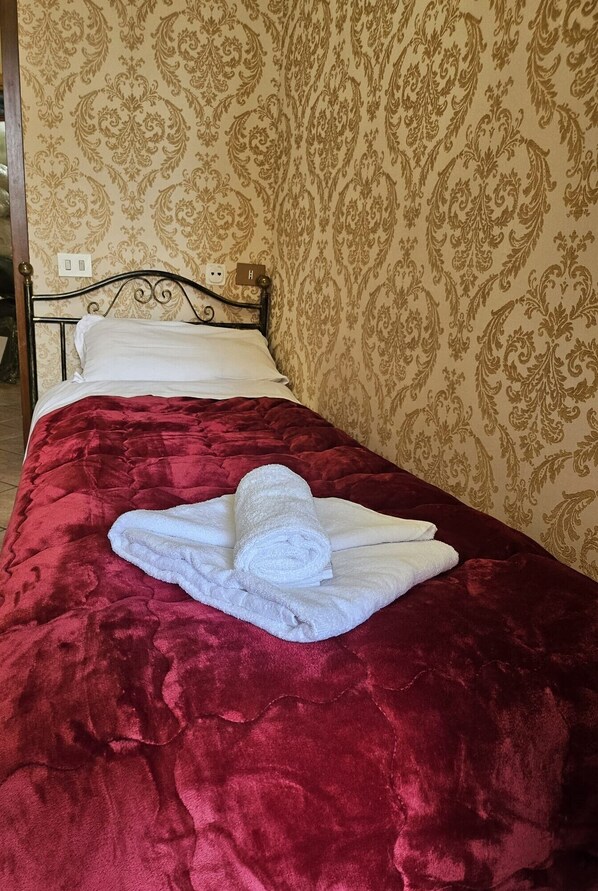 Una cama bien tendida con un edredón rojo y una toalla blanca enrollada encima.