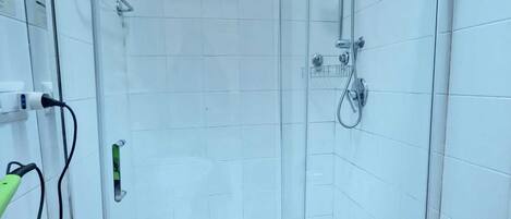 A bathroom with a glass-enclosed shower, white tiles, a white bathtub, and a white toilet.