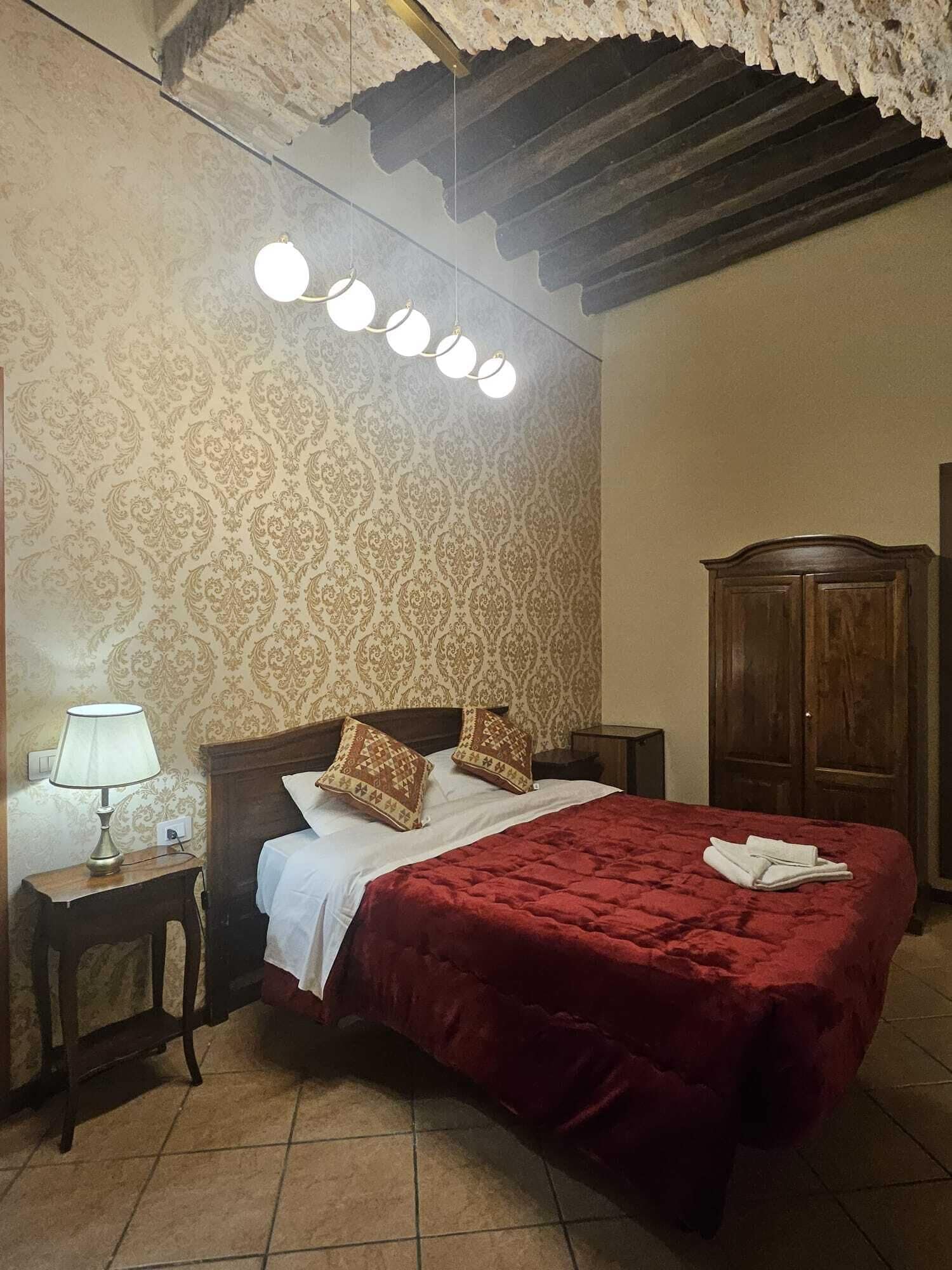 Een slaapkamer met een groot bed, een houten garderobe, een nachtkastje met een lamp en behang met een patroon.