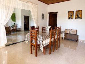 Un comedor con mantel a cuadros, sillas de madera, un jarrón con flores y un sofá con cojines.