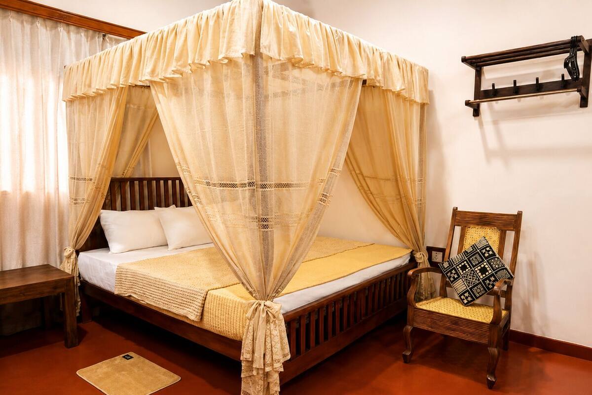 A bed with a canopy, a chair with a patterned cushion, a bedside table, and a wall-mounted shelf.