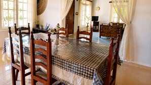 A dining area with a checkered tablecloth, wooden chairs, and a decorative wall hanging. - Aura Hilltop Matale (Matale)