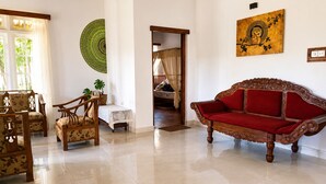A spacious room with a red sofa, wooden chairs, a small table, and a green wall hanging. - Aura Hilltop Matale (Matale)