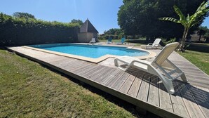 A rectangular swimming pool with a wooden deck and lounge chairs.