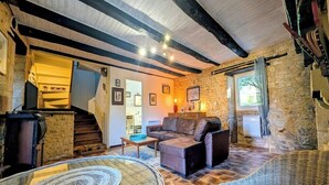 A rustic interior with stone walls, a wooden staircase, a sofa, and wicker furniture.