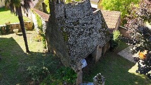 A stone structure with a sloped roof, surrounded by greenery and a small garden area.