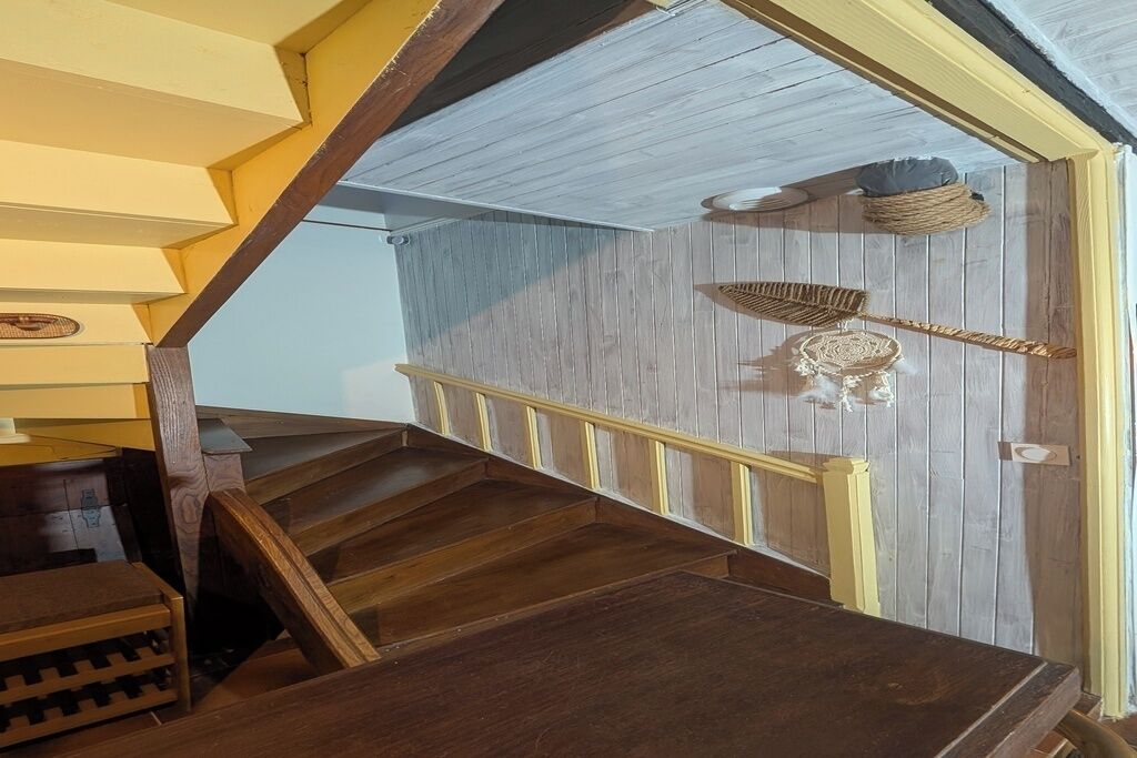 Eine Holztreppe mit Geländer, eine Wand mit dekorativem Muster und ein kleiner Tisch mit einem Korb auf der Landung.