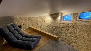 Een slaapkamer met zolder, met een stenen muur, een houten platform en een donkerblauwe bank.