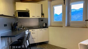 Een praktische keuken met een magnetron, fornuis en kastjes. Twee ramen bieden uitzicht op bergen.